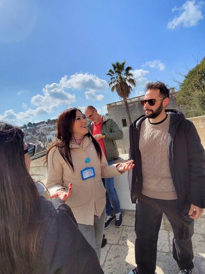A group of people standing outdoors, engaged in conversation, with a clear sky and palm trees in the background. 4
