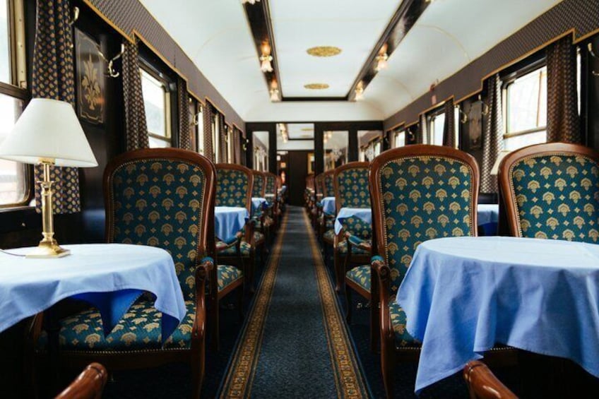 Vagon restaurante de tren con manteles azules, sillas estampadas y pasillo alfombrado. 1