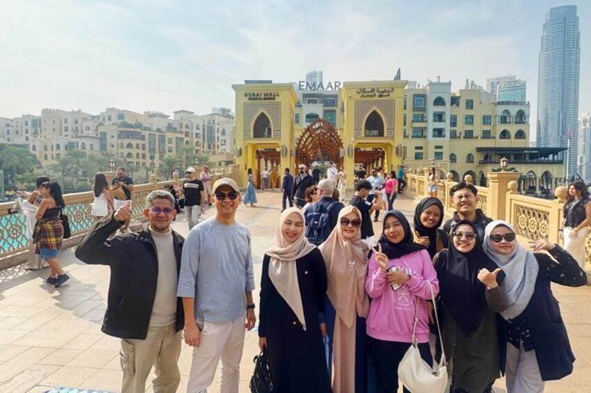 Un grupo de personas posando frente a un edificio con un arco grande y un letrero que dice 'DUBAI MALL EEMAAR'. 4