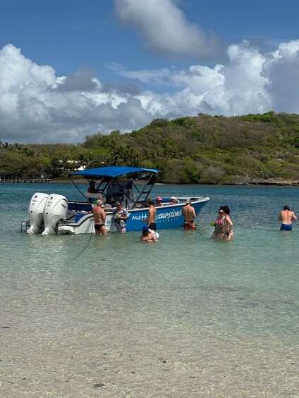 A boat docked at a beach with people in the water and a forested hill in the background. 2