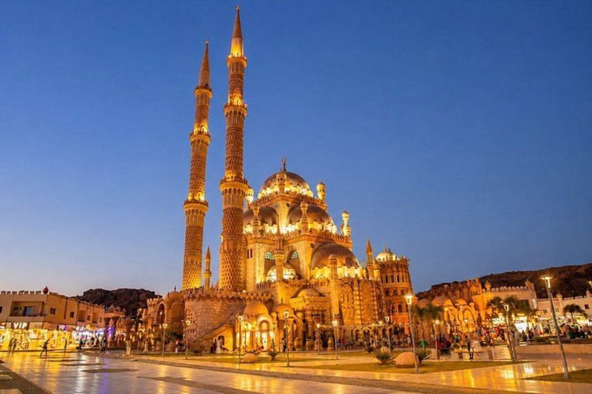 A mosque with two tall minarets and a large dome, surrounded by a plaza with people. 1