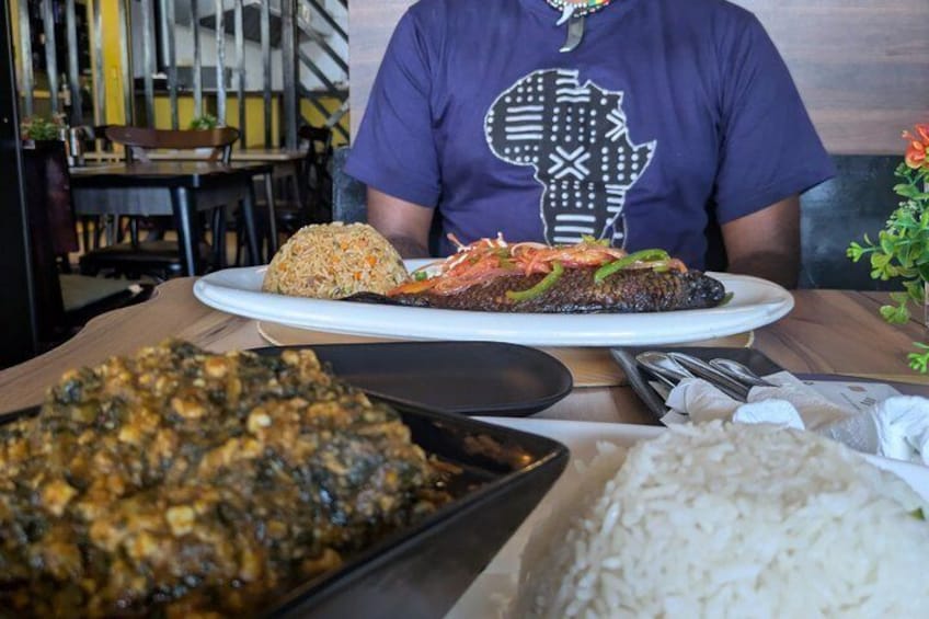 A person seated at a table with a plate of food, including rice, a meat dish, and a side of greens. 5