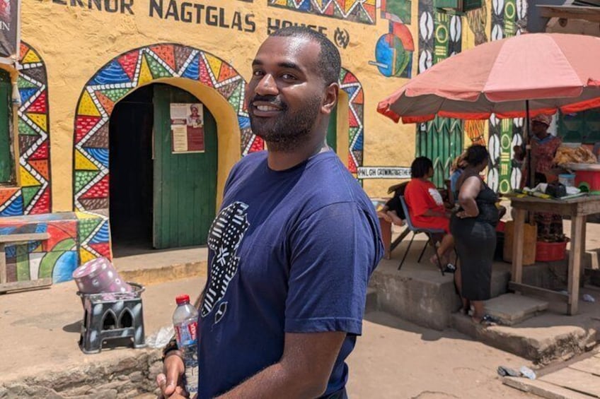 A man standing in front of a colorful building with a sign that reads 'NAGTLAS HOUSE.' 2