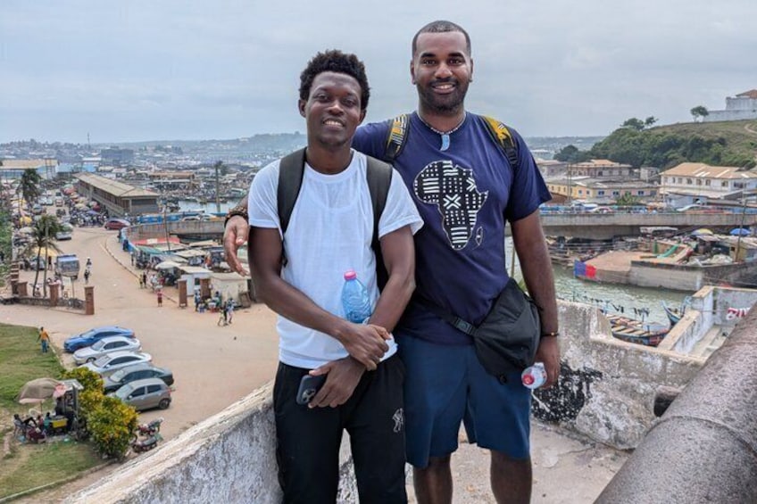 Two people standing on a high vantage point overlooking a cityscape with buildings, roads, and a body of water. 4