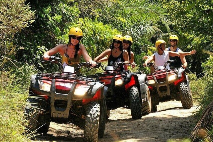 Quatre personnes conduisent des quads sur un chemin de terre, entourés de verdure. 1