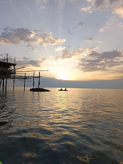 A sunset over a calm sea with a pier and a small boat with people. 3