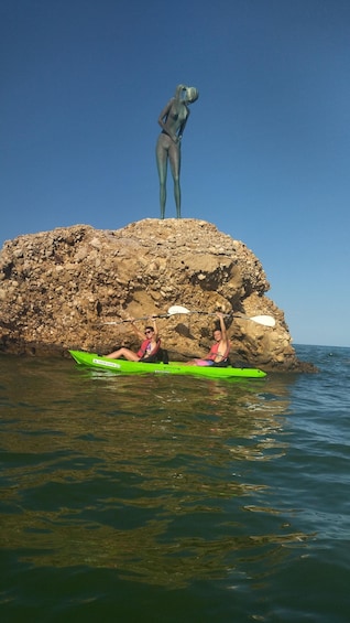 A green kayak on calm water, a rocky outcrop, and a statue of a figure. 5