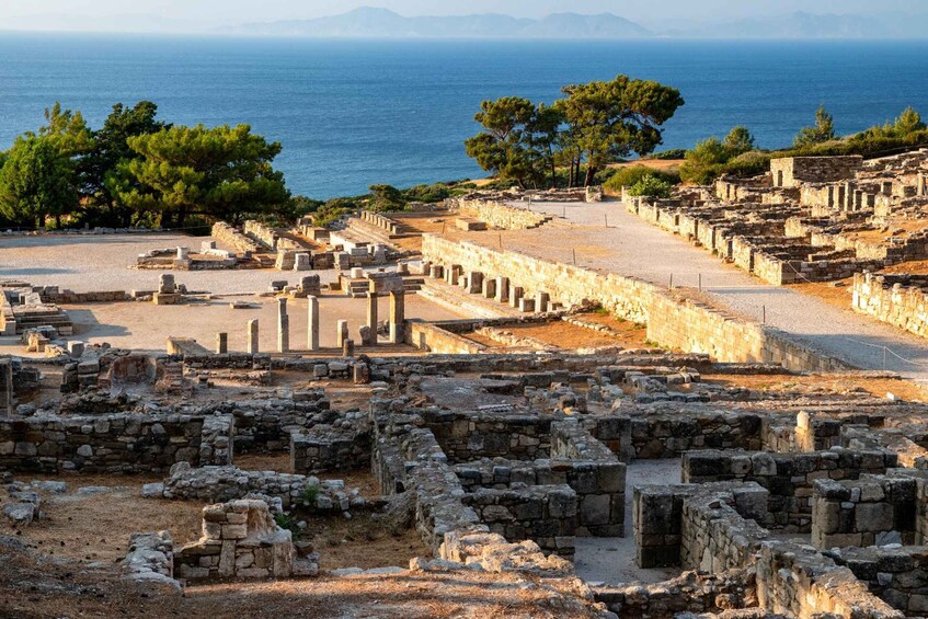Ancient ruins with stone columns and walls, a clear sky, and the sea in the background. 1