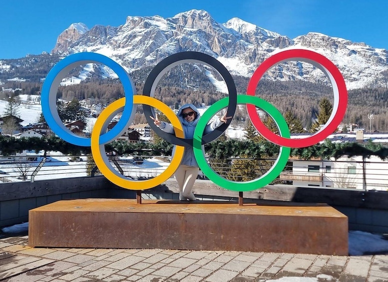 A person standing in front of Olympic rings with a mountainous backdrop. 2