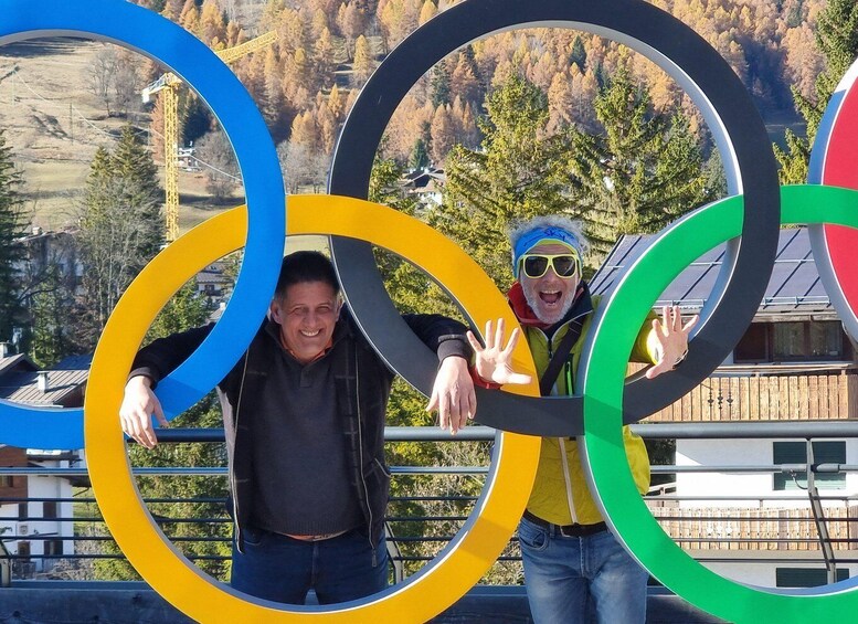 Two people holding Olympic rings, with a mountainous landscape in the background. 4