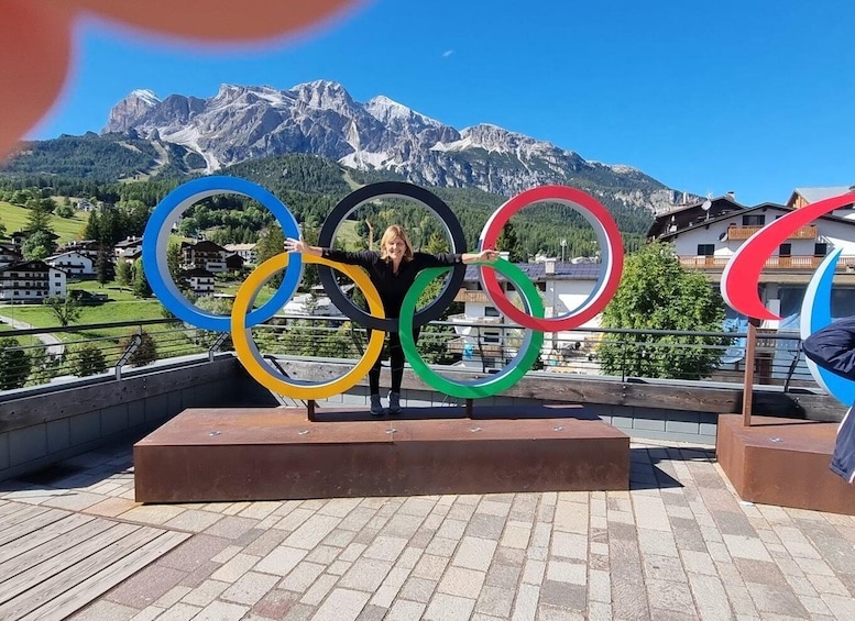 A person holding Olympic rings on a rooftop with a mountain backdrop. 3