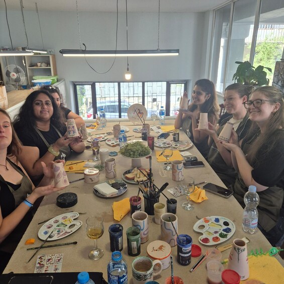 A group of people sitting around a table with various items like plates, cups, and paint supplies. 3