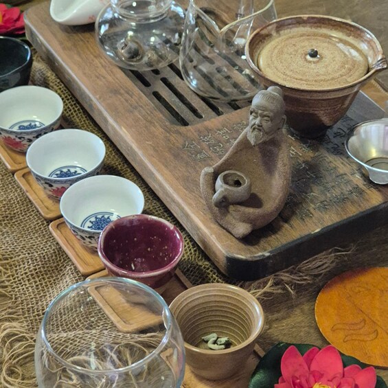 A traditional tea set with cups, a teapot, and a stone statue on a wooden tray. 2