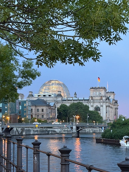 A river with a bridge, a boat, and a large building with a dome and flags. 5