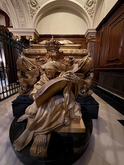 A detailed sculpture of a seated figure with a crown, surrounded by ornate carvings and a grand architectural ceiling. 3