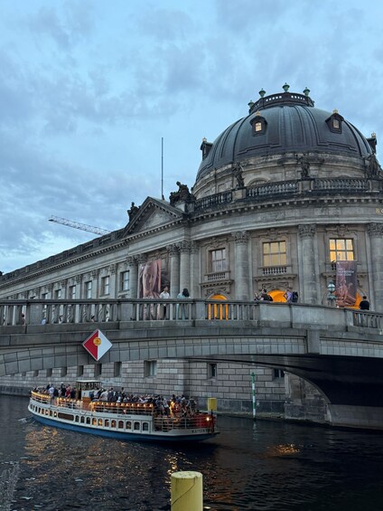 A historic building with a large dome and classical architecture, a bridge with people walking, and a boat with passengers on a river. 4