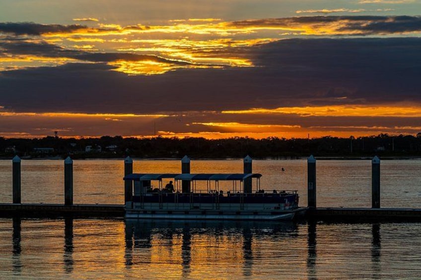 Een zonsondergang boven het water, met een boot afgemeerd aan een steiger. 5