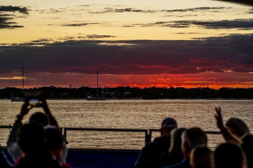Een zonsondergang boven het water, met zeilboten en mensen in een boot. 3