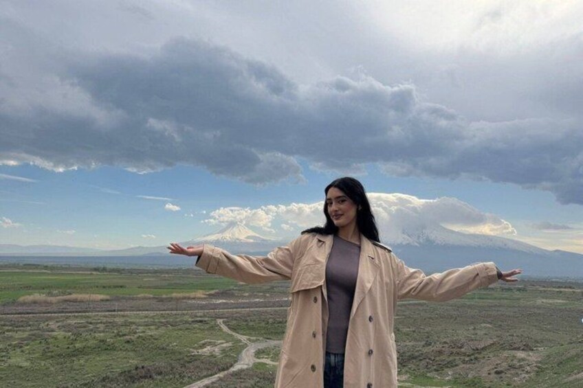 Una persona de pie con los brazos extendidos en un paisaje extenso, con una montaña al fondo. 1