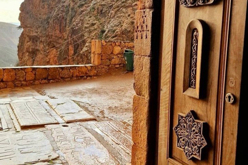 A stone wall, a wooden door with intricate carvings, and a stone floor with patterns. 2