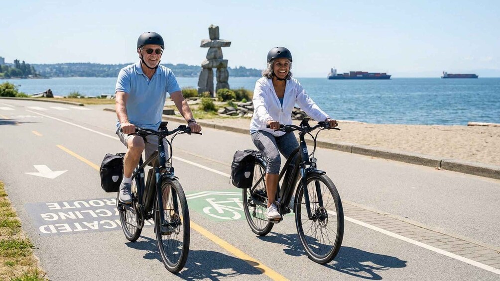 Two people riding bicycles on a road with a bike lane, near a body of water and a large statue. 4