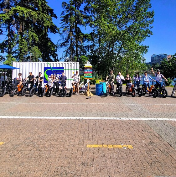A group of people on bicycles lined up on a paved path with trees and a signboard in the background. 5