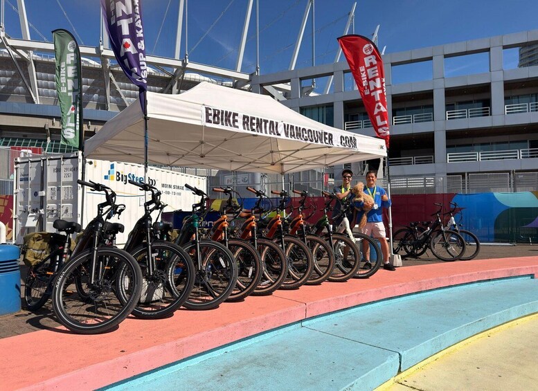 A bike rental station with a canopy labeled 'EBIKE RENTAL VANCOUVER' and several bicycles lined up. 1