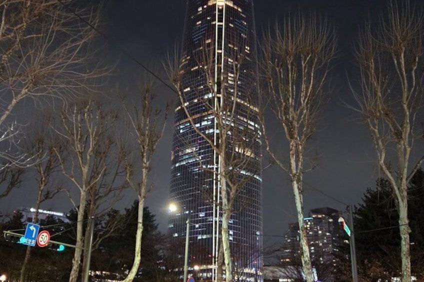 Un rascacielos alto e iluminado de noche, con árboles despojados en primer plano. 3