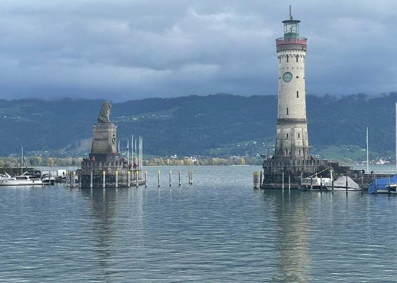 A lighthouse and a statue on a pier with boats in the water and hills in the background. 2