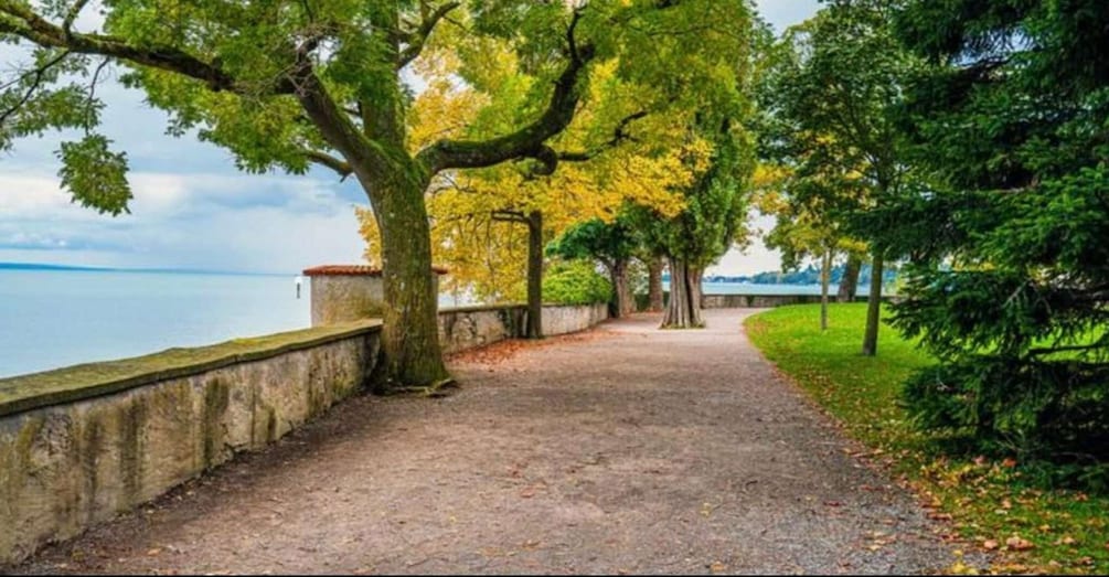 A gravel path beside a body of water, lined with trees and a stone wall. 3