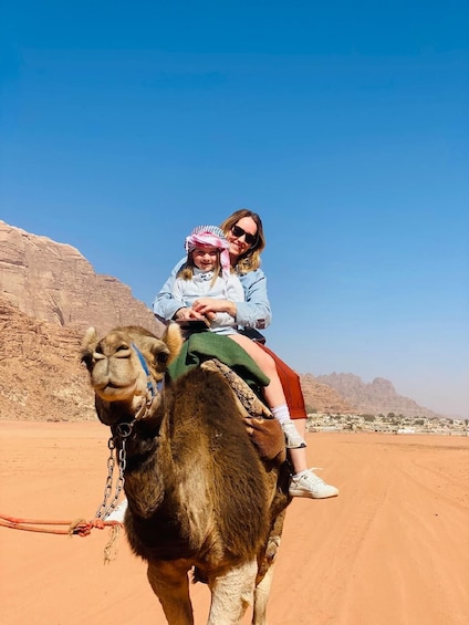 A camel with a rider and a guide in a desert landscape. 4