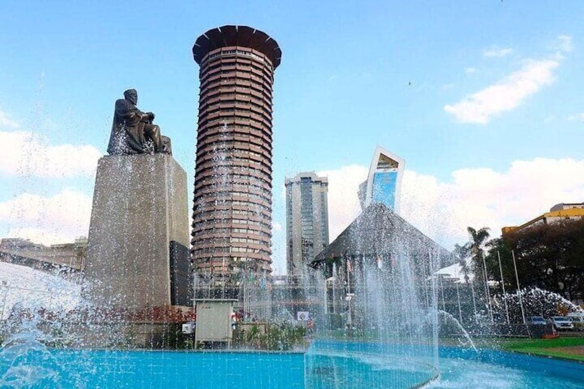 Paesaggio urbano con un alto edificio cilindrico, una statua e una fontana. 1