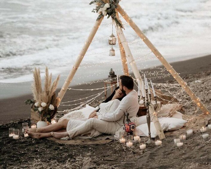 A couple relaxing under a tent on a beach with candles and flowers. 2