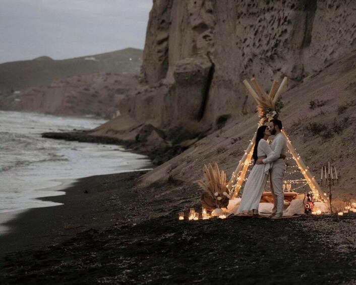 A couple embracing on a beach with a teepee and string lights. 1