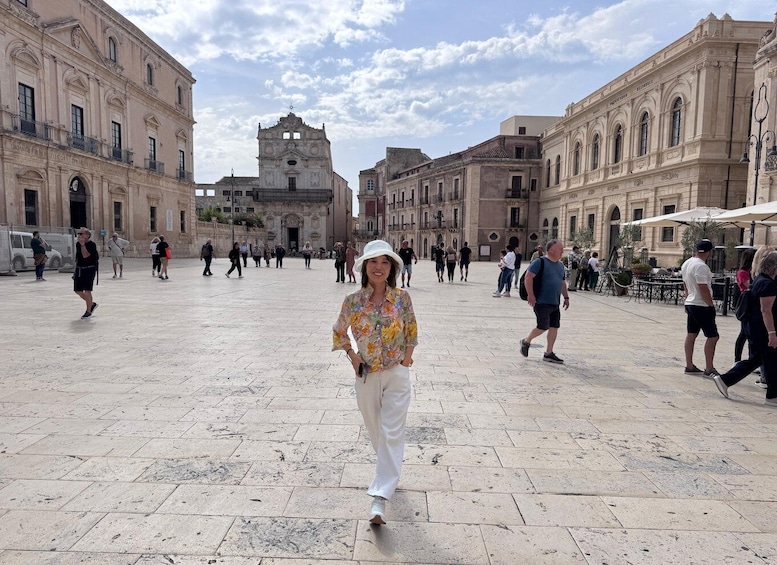 Una plaza histórica con arquitectura clásica, un edificio central con un campanario, y gente caminando. 1