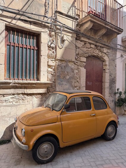Un coche amarillo antiguo estacionado frente a un edificio desgastado con una ventana con barrotes y una puerta roja. 2