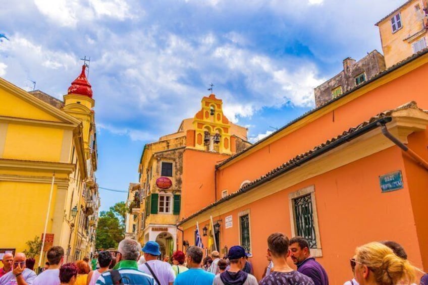 A crowded street with colorful buildings, a prominent church with a red dome, and a clear blue sky. 1