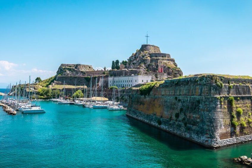 A coastal fortification with a church, a lighthouse, and a clear blue sea. 3