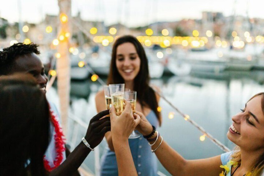 People toasting with drinks at a waterfront with string lights. 1