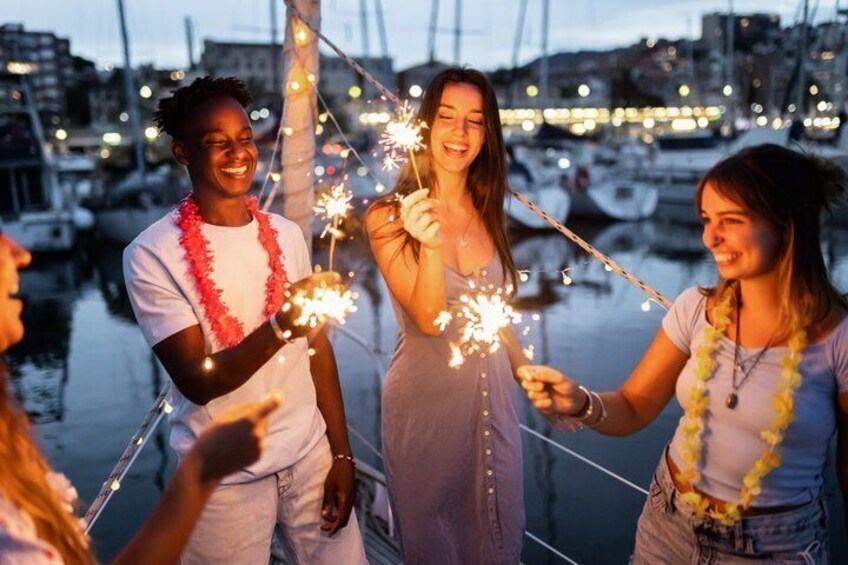A group of people holding sparklers by a marina with boats in the background. 5