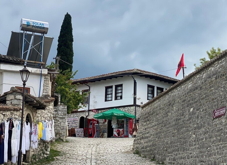 A cobblestone street with a white building, a solar power sign, and a red flag. 4