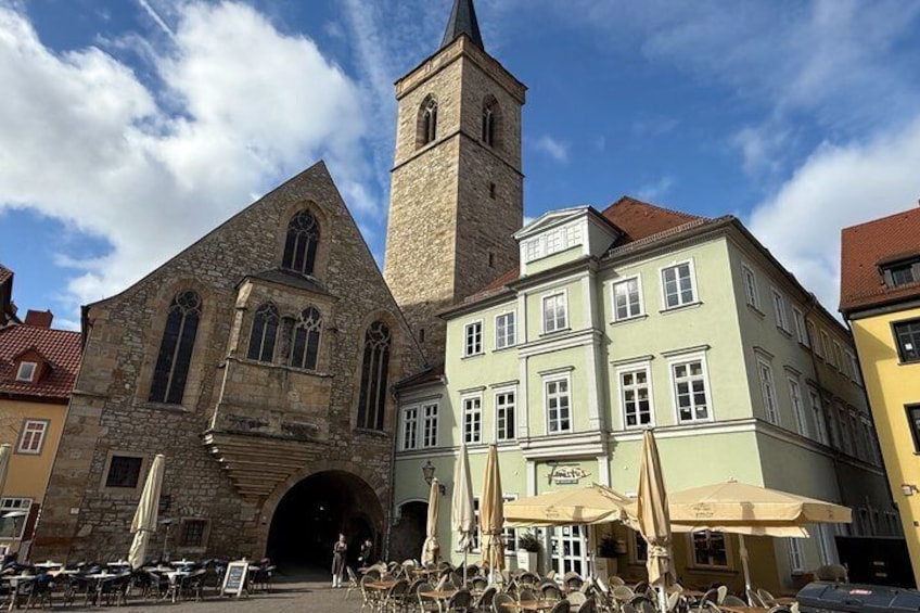 A historic church with a tall tower, a café with outdoor seating, and a cobblestone street. 1
