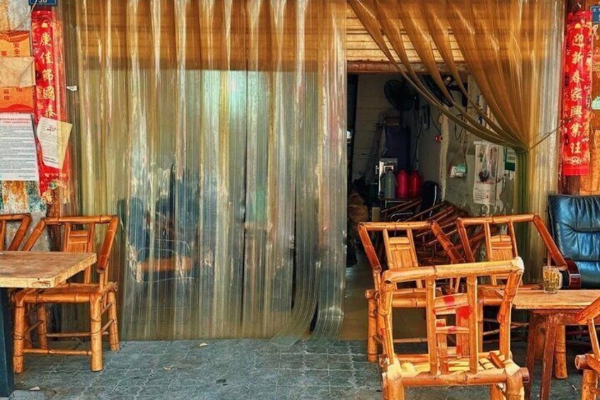 A rustic wooden furniture shop with bamboo chairs and tables, a corrugated metal wall, and red decorations. 4