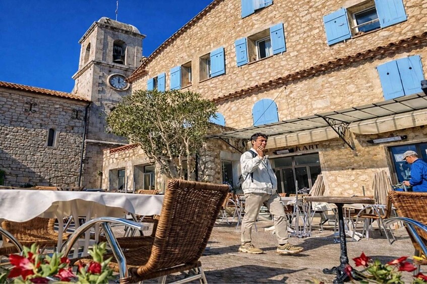 A stone building with blue shutters, a clock tower, and outdoor seating. 1