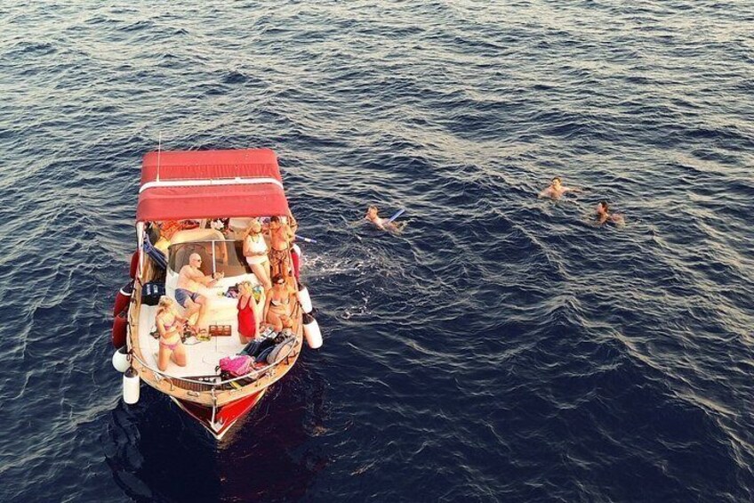 En båt med folk ombord och personer som simmar i vattnet. 2
