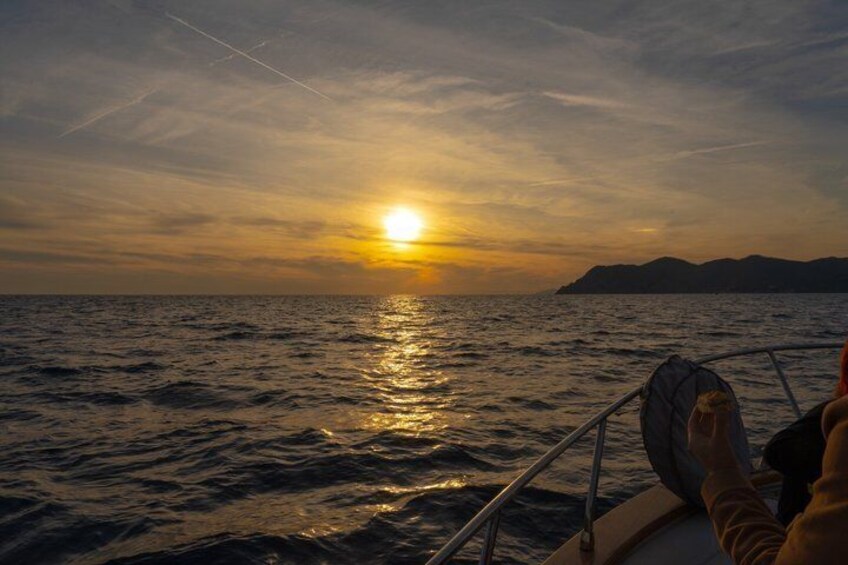 A sunset over the ocean with a boat and mountains in the distance. 1