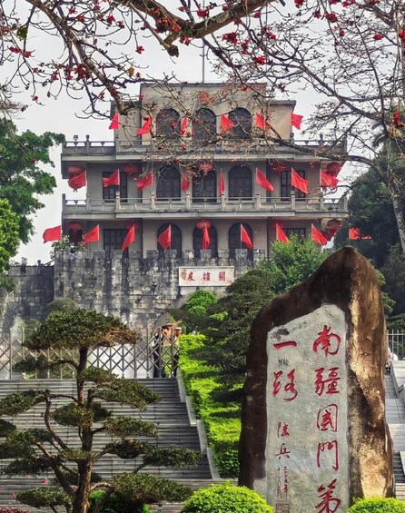 A traditional building with red flags, a stone monument with inscriptions, and a staircase leading up to it. 3