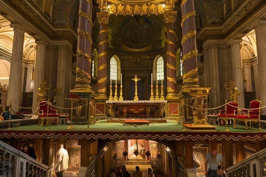 An ornate church interior with a central altar, golden columns, and red chairs. 2