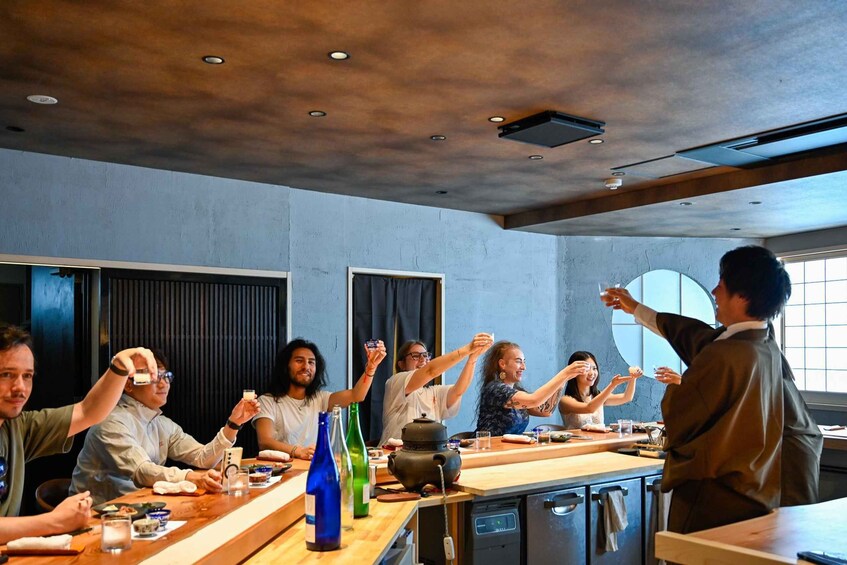 A group of people seated around a long table in a modern dining setting with a chef standing by. 4