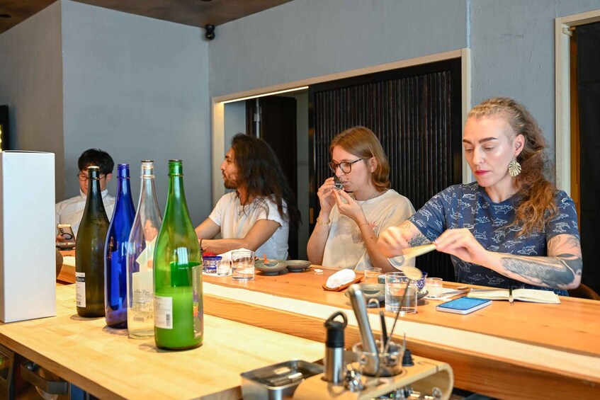 A group of people seated at a wooden table with wine bottles and glasses. 3